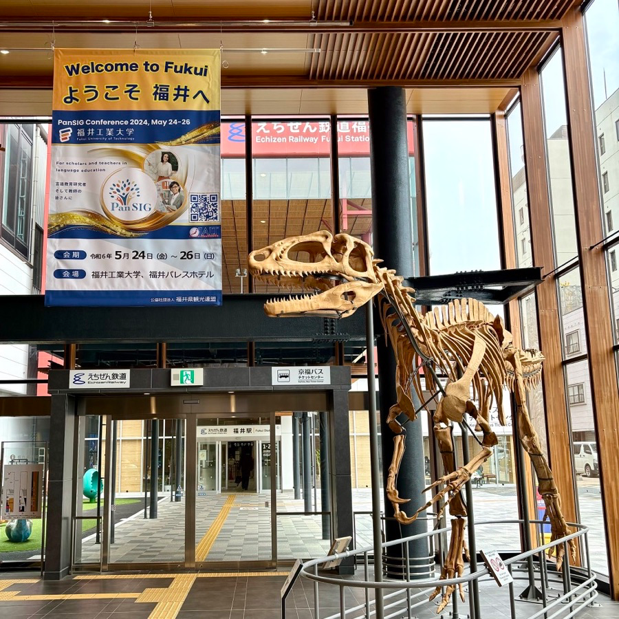 banner welcoming PanSIG participants to Fukui, hanging near a dinosaur skeleton in Fukui Station